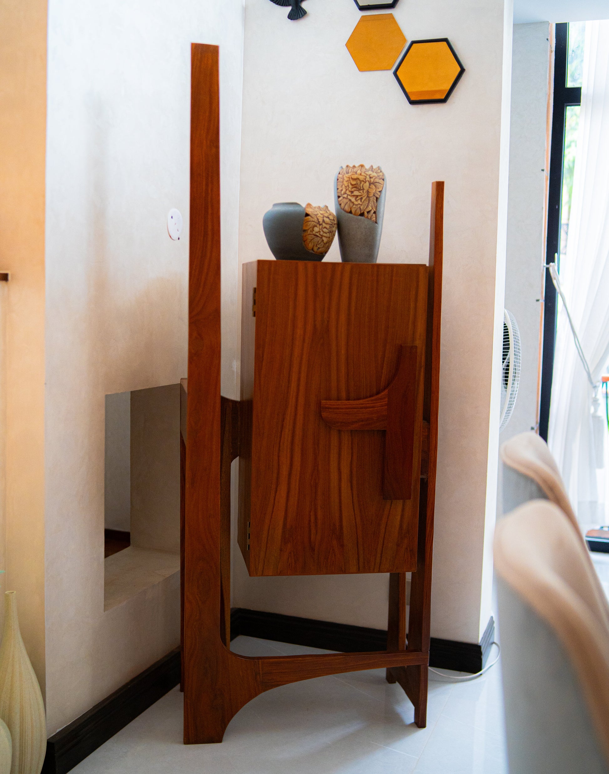 Wooden cabinet with decorative items against a wall with geometric wall art.